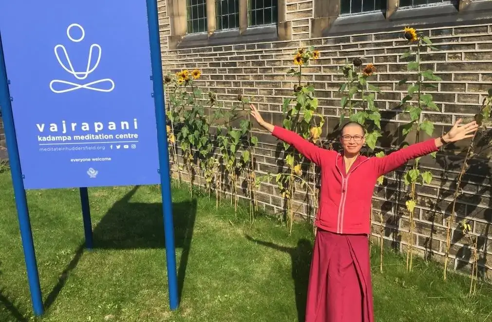 Kelsang Varahi, a Buddhist nun, standing outside Vajrapani Buddhist centre in Huddersfield, with her arms outstretched in a welcoming fashion with a happy smiling expression.