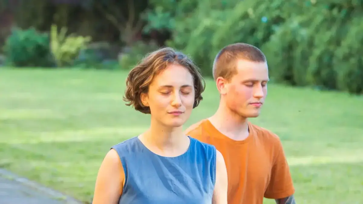 Two people, a young woman and man, eyes closed, peacefully in meditation outdoors