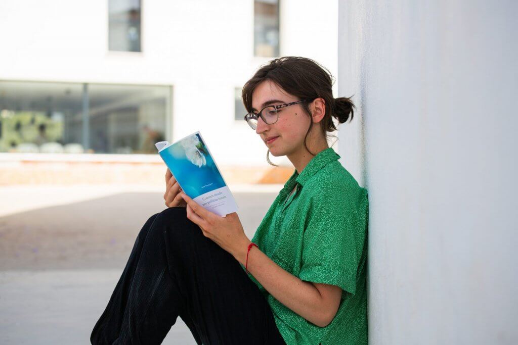 A young woman with glasses reading a Buddhist text written by Geshe Kelsang Gyatso, concentrating on what she is reading.