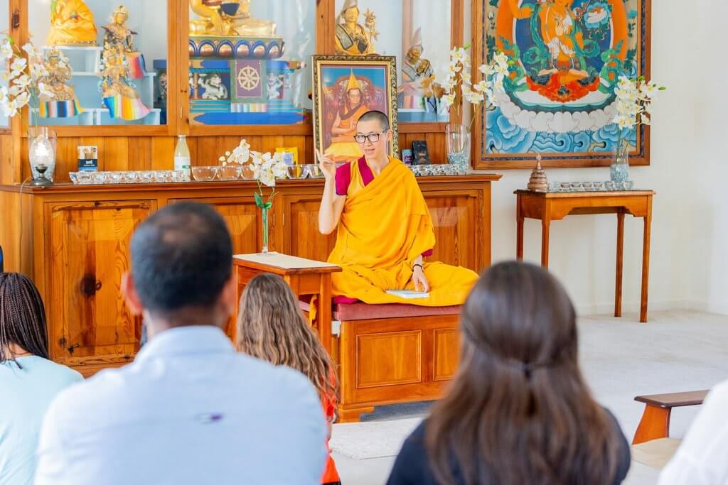 Buddhist Nun, Gen Kelsang Varahi, teaching about Buddhism and meditation to a group of people in front of a traditional buddhist shrine with statues and offerings